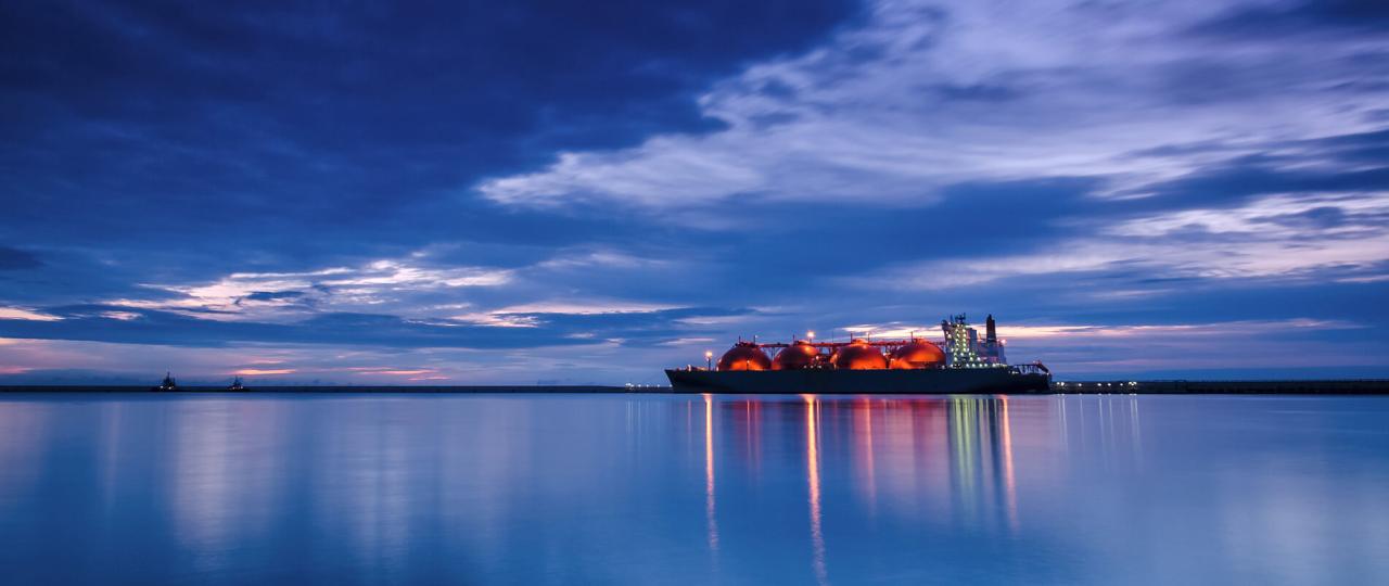 Sicht vom Meeresspiegel aus auf die Lichter des LNG-Frachters Arctic Voyager, die sich im Hafen während der Dämmerung auf dem Wasser spiegeln.